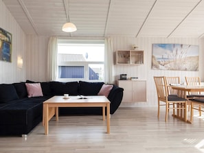 A modern living room with a black sofa, wooden coffee table, and a dining table with chairs.
