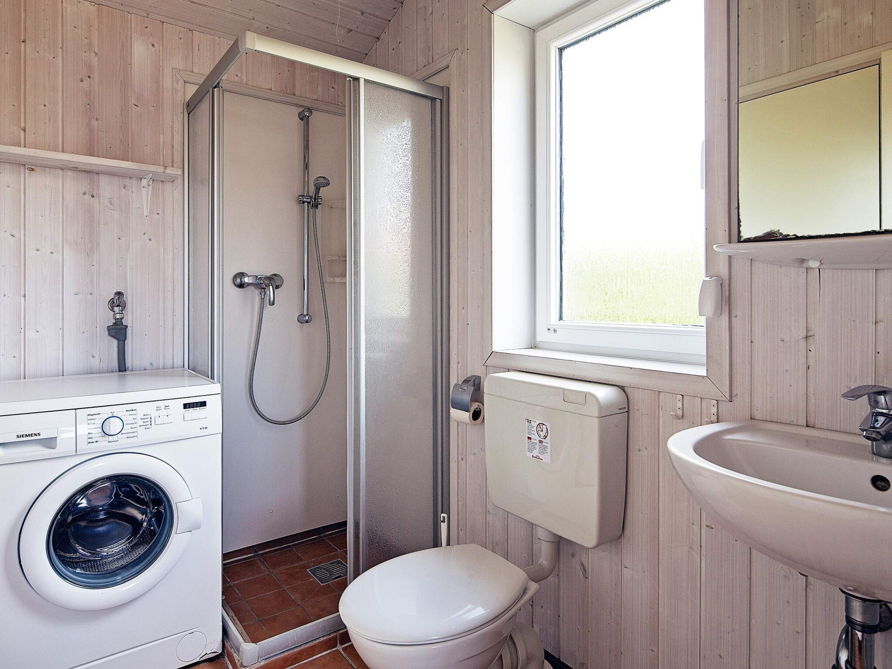 A compact bathroom with a washing machine, a toilet, a shower, and a sink.