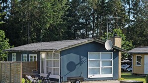 A small, single-story building with a satellite dish, a covered patio with chairs, and a wheelbarrow. - 5 Person Holiday Home in Ans By-by Traum (Ans)