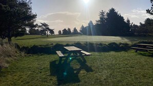 Um campo gramado com uma mesa de piquenique e um campo de golfe ao fundo.