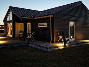 A modern wooden house with a sloped roof, a covered porch, and a small outdoor seating area with chairs. - 5 Star Holiday Home in Brovst (Brovst)