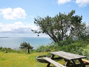 A picnic table with benches, a small fire pit, and a view of the water. - 6 Person Holiday Home in Spottrup (Spøttrup)