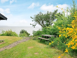 A picnic area with a view of the sea, surrounded by greenery and yellow flowers. - 6 Person Holiday Home in Spottrup (Spøttrup)