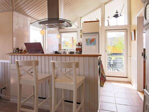 Een keuken met een houten bar, twee witte barstoelen, een kaart aan de muur en uitzicht buiten door een glazen deur.