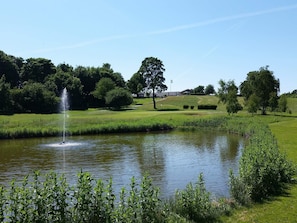 A tranquil pond with a fountain, surrounded by lush greenery and a golf course in the background. - 5 Star Holiday Home in Jaegerspris (Jægerspris)