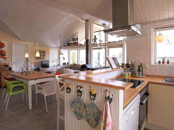 A spacious kitchen with a wooden island, a dining area with chairs, and a living room with a sofa and fireplace. - 5 Star Holiday Home in Jaegerspris (Jægerspris)