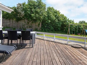 A wooden deck with outdoor furniture, a swing set, and a white fence. - 4 Star Holiday Home in Ebeltoft (Ebeltoft)