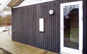 Een gebouw met een donkere gevel, een witte deur met ruitpanelen en een klein rechthoekig raam.