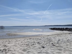 Una playa con muelle de madera, agua tranquila y cielo despejado.