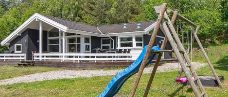 A cabin with a deck, a blue slide, and a wooden swing set.