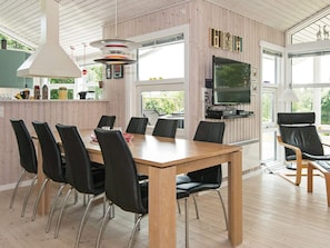 Un comedor moderno con una mesa de madera y sillas negras, un televisor montado en la pared y un ventanal que proporciona luz natural.