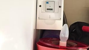 Un récipient rouge doté d’un couvercle, contenant un objet blanc à l’intérieur, peut-être un ustensile, dans une pièce dont le mur et la porte sont blancs.