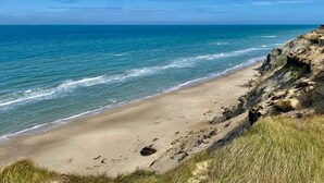 Une plage avec une eau d’un bleu limpide, un rivage sablonneux et des falaises rocheuses.