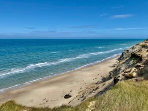A beach with clear blue water, sandy shore, and rocky cliffs.