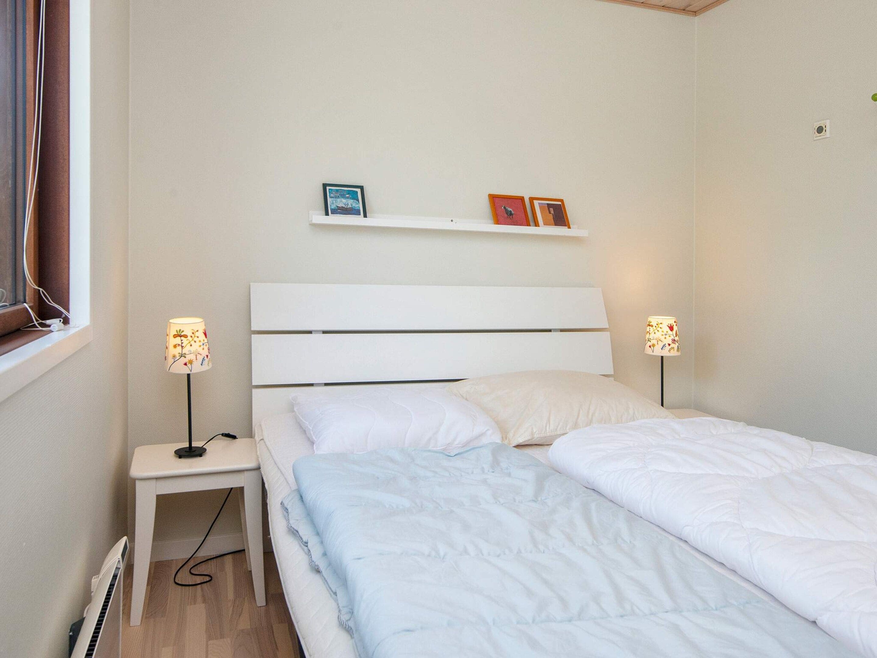 A bedroom with a white bed, bedside tables, and wall-mounted shelves with pictures.