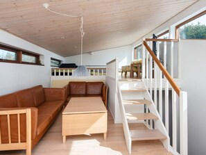 A modern interior with a wooden ceiling, a brown leather sofa, a wooden table, and a staircase with white railings. - 4 Star Holiday Home in Bjert (Bjert)
