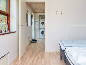 A bedroom with a bed, a wooden floor, a washing machine, and a window with red flowers. - 4 Star Holiday Home in Bjert (Bjert)
