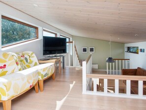 A modern living room with a flat-screen TV, a sofa with a leaf-patterned cover, a wooden bench, and a staircase with a railing. - 4 Star Holiday Home in Bjert (Bjert)