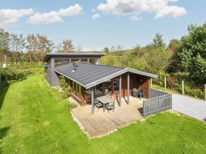 A modern house with a deck, a covered patio, and a large window overlooking a grassy yard. - 4 Star Holiday Home in Bjert (Bjert)