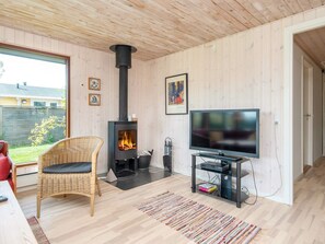 A modern living room with a wood-burning stove, a television, and a wicker chair. - 4 Star Holiday Home in Bjert (Bjert)