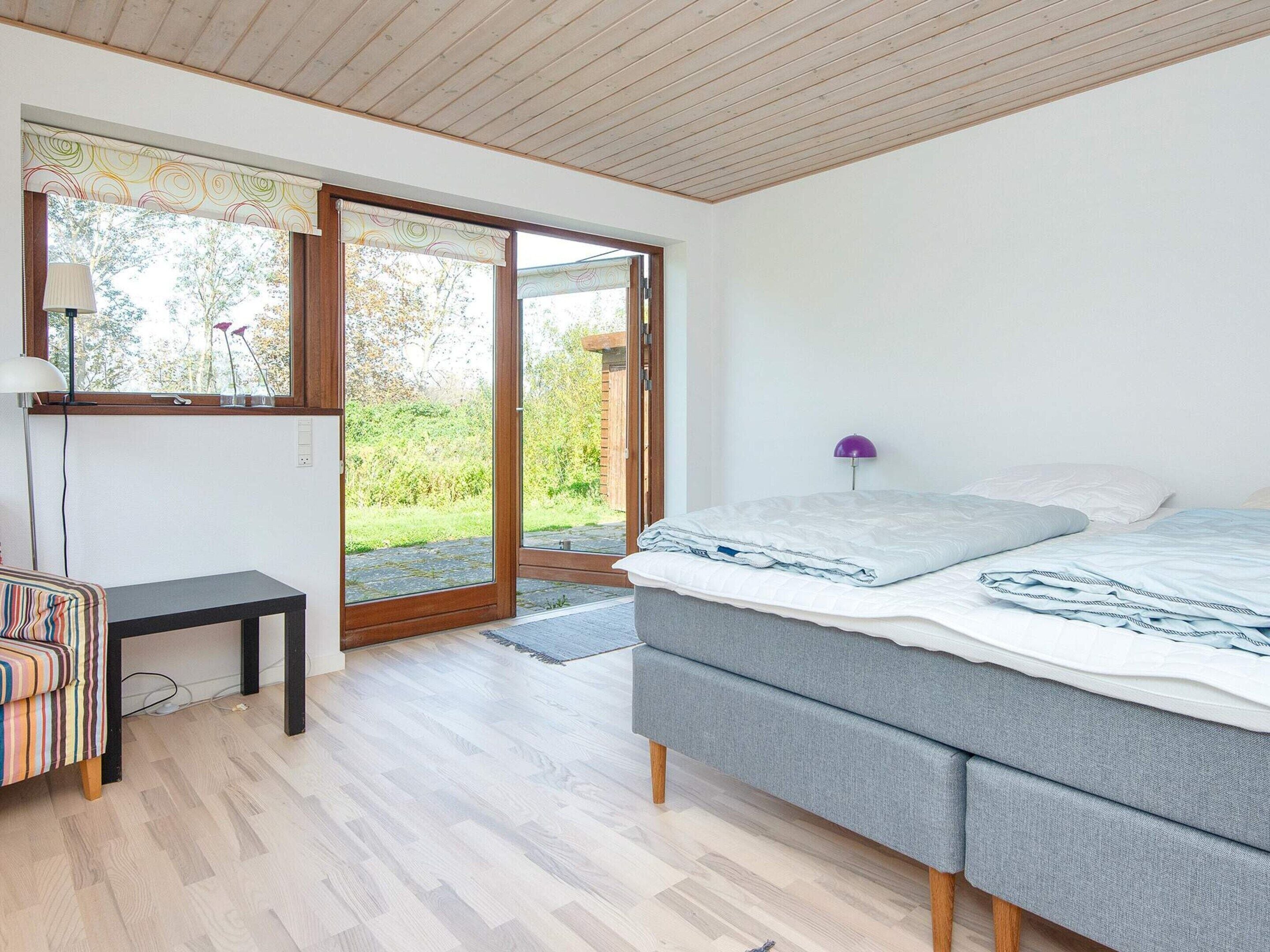 A bedroom with a bed, a desk, and a view of the outdoors.