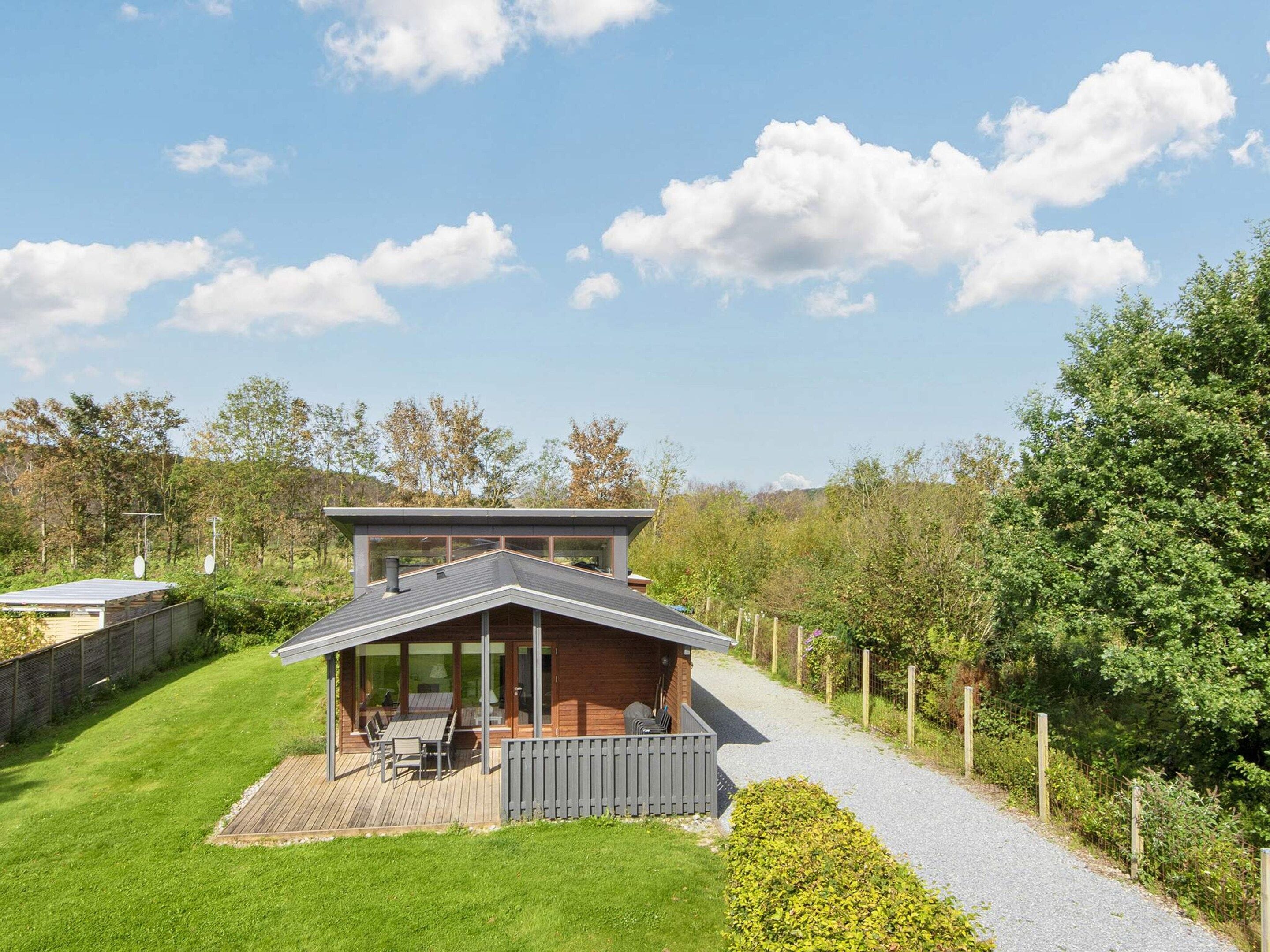 Une maison moderne dotée d’une terrasse, entourée d’une pelouse bien entretenue et d’un chemin de gravier.