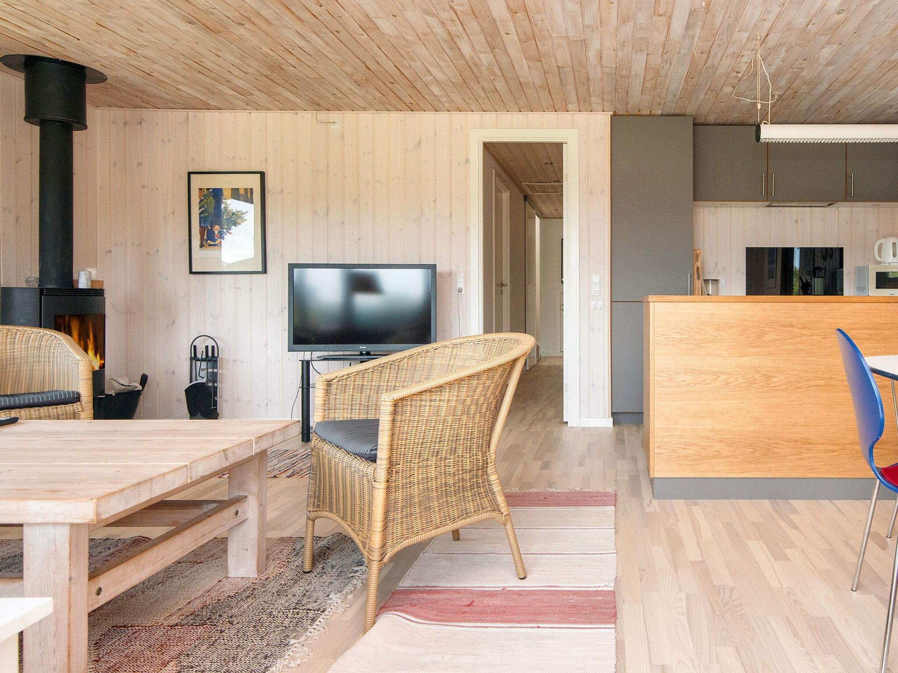 A modern living room with a fireplace, a television, wicker furniture, and a kitchen area.