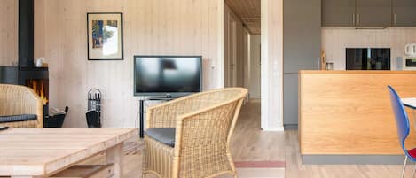 A modern living room with a fireplace, a television, wicker furniture, and a kitchen area.