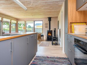 A modern kitchen with a central island, a fireplace, and a view through large windows. - 4 Star Holiday Home in Bjert (Bjert)