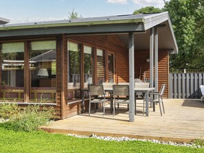 A wooden house with a covered patio area featuring a table and chairs. - 4 Star Holiday Home in Bjert (Bjert)