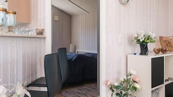 Una habitación con cama, una silla, un escritorio con computadora, un reloj y un florero con flores.