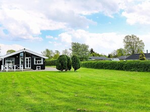 Ein modernes Haus mit großem Rasen, umzäunter Terrasse und gepflegtem Heckenstreifen.