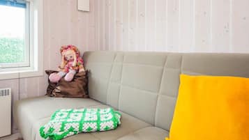 A room with a beige sofa, a window, a doll, and a green and white patterned blanket.