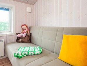 A room with a beige sofa, a window, a doll, and a green and white patterned blanket.
