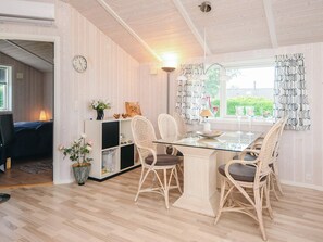 A dining area with a glass table, wicker chairs, a white cabinet with decorative items, and a view through the window.