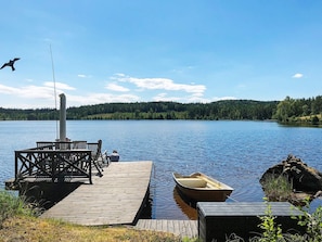 En träbrygga som sträcker sig ut i en stilla sjö, med en roddbåt och ett fiskespö.