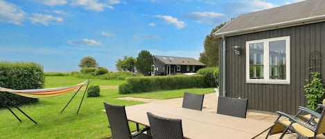Un patio exterior con mesa y sillas, una hamaca y vistas a una casa y al paisaje.