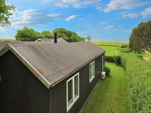 A single-story building with a sloped roof, a small attached garage, and a clear view of a grassy field and trees in the background.