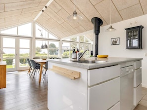 A modern kitchen with a large island, white cabinetry, and a view through large windows. - 4 Star Holiday Home in Nysted (Nysted)