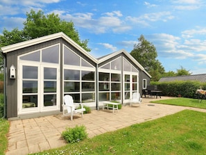 A two-story house with large windows, a patio with outdoor furniture, and a well-maintained lawn.