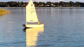 A sailboat with a registration number on the sail, floating on calm water with a shoreline in the background. - 4 Star Holiday Home in Nysted (Nysted)