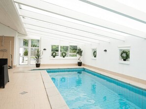 A swimming pool with tiled edges, potted plants, and a white interior.