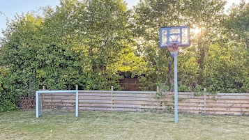 A basketball hoop in a backyard with a wooden fence and trees in the background.