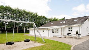 A white building with a sloped roof, a swing set, and a paved area with benches. - 5 Star Holiday Home in Ega (Aarhus)