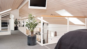 Un interior moderno con un televisor de techo grande, una planta en maceta y vistas del cielo a través de tragaluces.