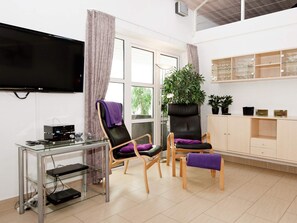 A modern living room with a flat-screen TV, two leather chairs, a glass coffee table, a potted plant, and a wooden cabinet with glassware. - 5 Star Holiday Home in Ega (Aarhus)