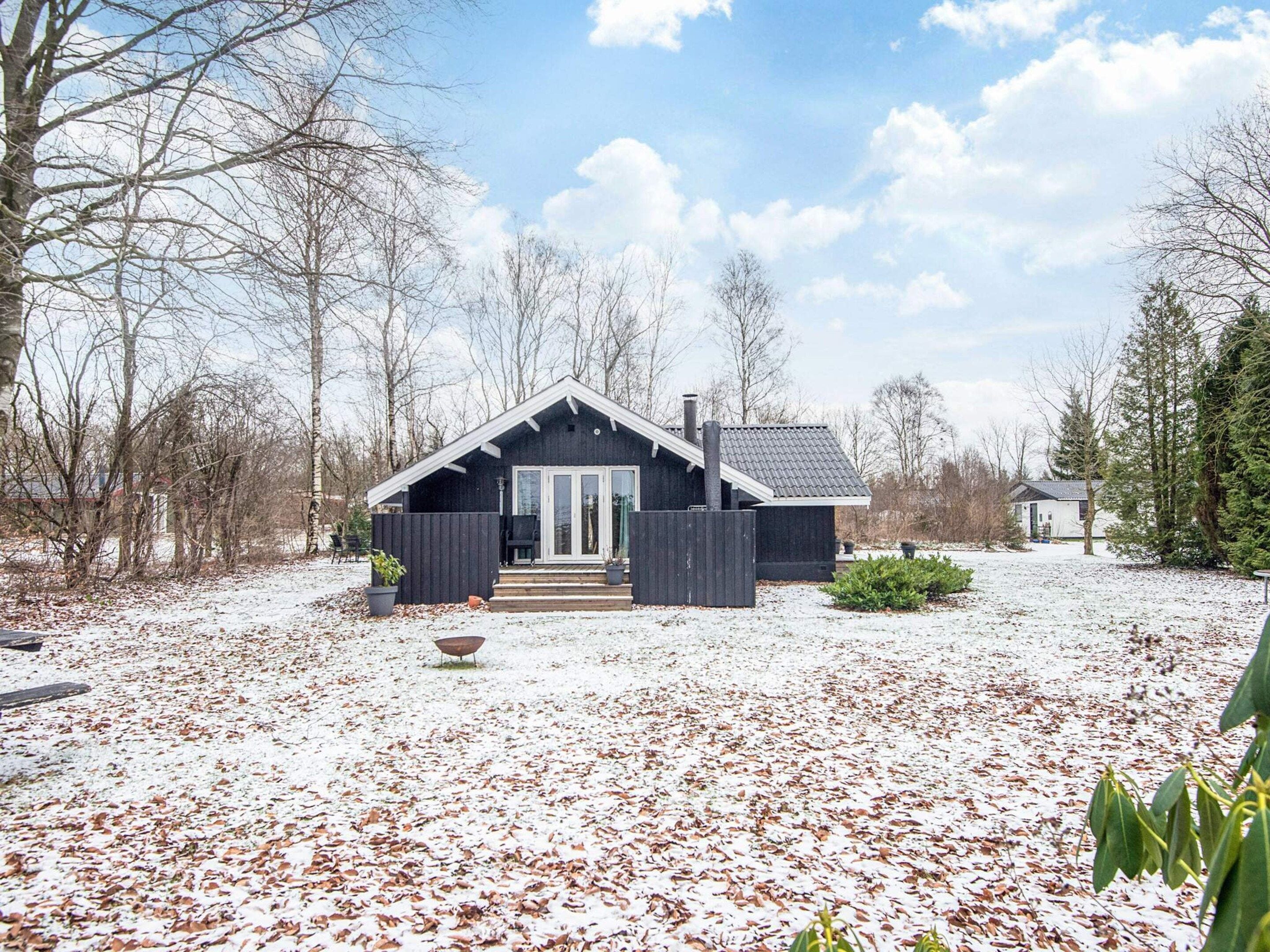 A cabin with a dark exterior, a front porch, and a snow-covered yard.