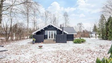 A cabin with a dark exterior, a front porch, and a snow-covered yard.