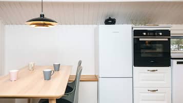 Eine kleine Küche mit Esstisch, Stühlen, Kühlschrank, Backofen und einer Pendelleuchte.