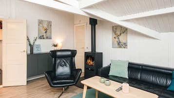 Una sala de estar acogedora con un sillón de cuero negro, un sofá negro, una mesa de centro de madera y un estufa de leña negra.
